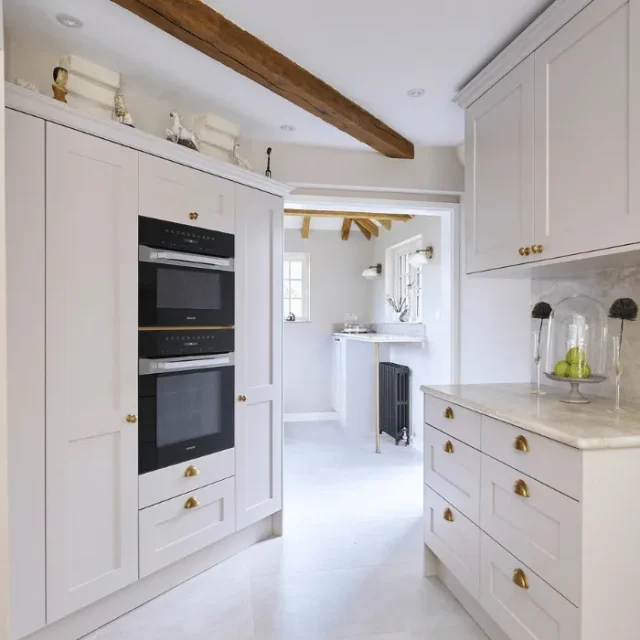light pink cottage kitchen with angular wall units with integrated appliances and beam detail